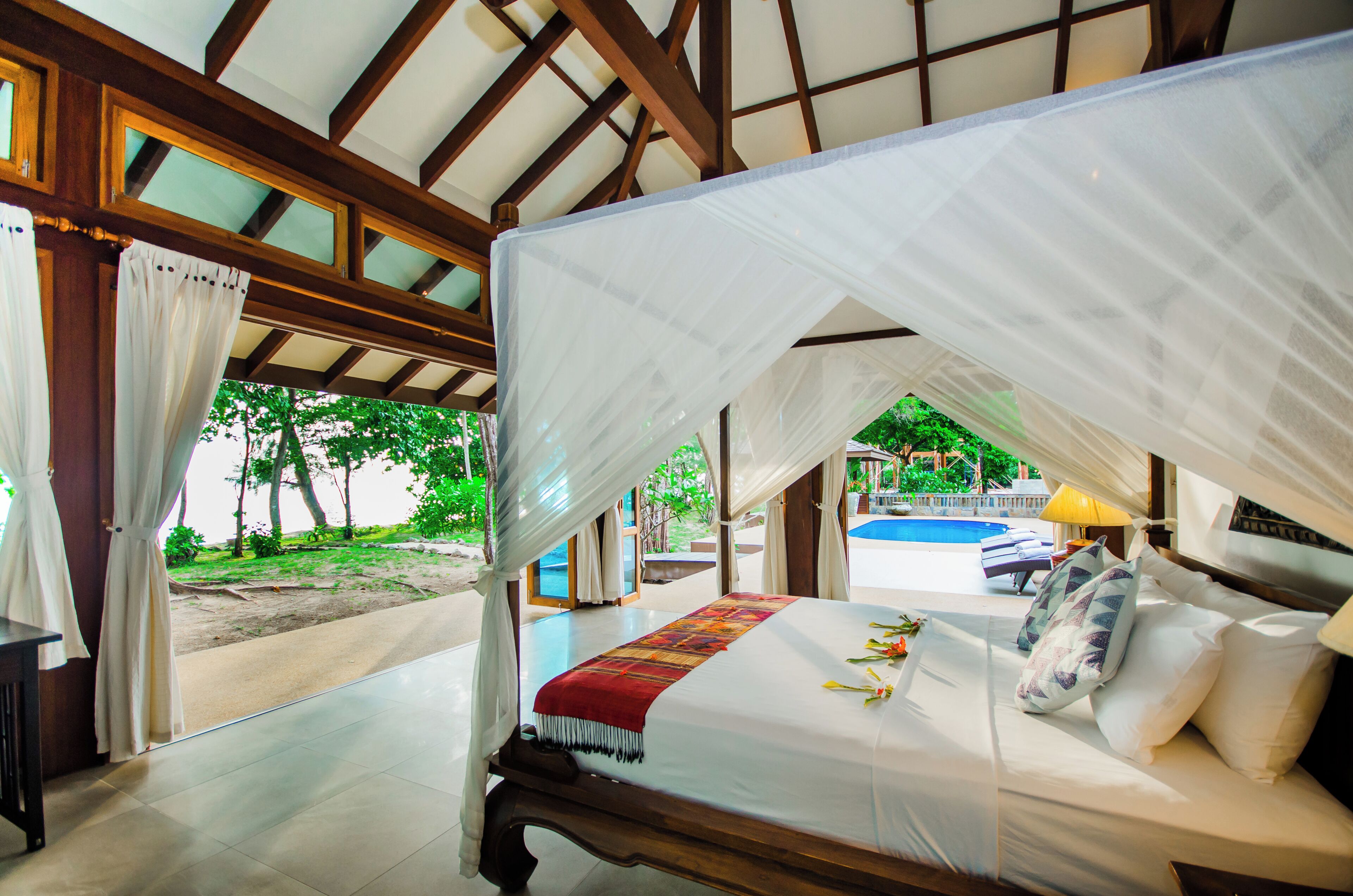 A room with a bed, a view of a swimming pool, and a covered outdoor area.