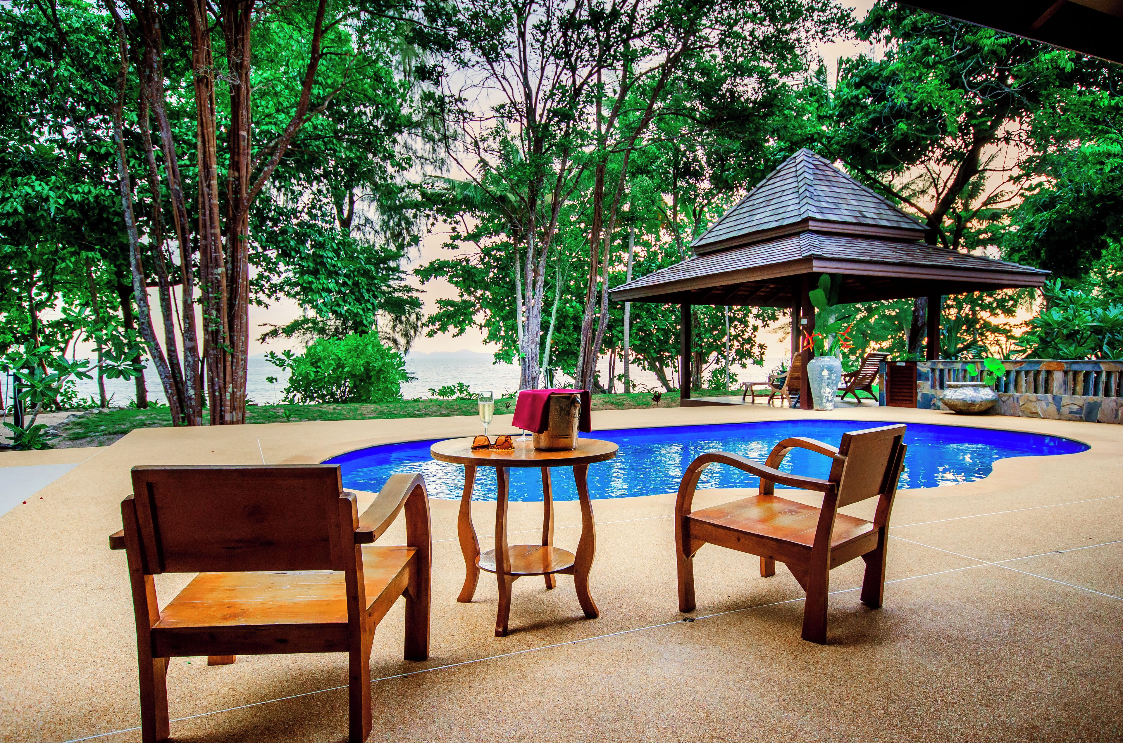 A pool area with wooden chairs and a gazebo.