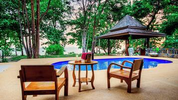 A pool area with wooden chairs and a gazebo.