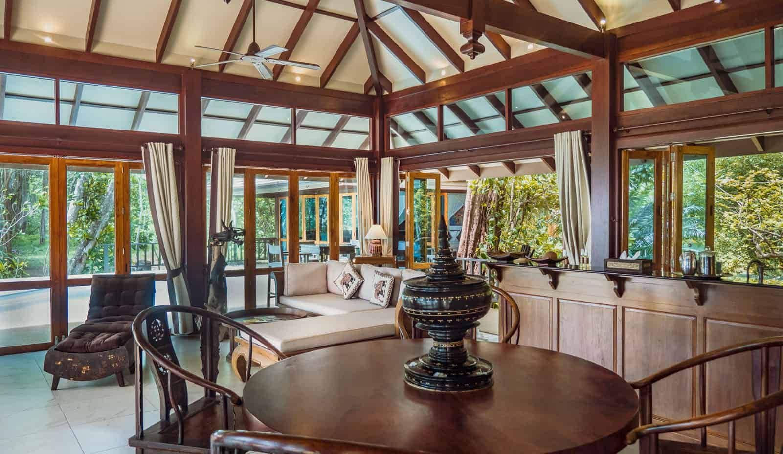 A spacious room with a high ceiling, large windows, a round wooden table, and a seating area with a sofa and chairs.