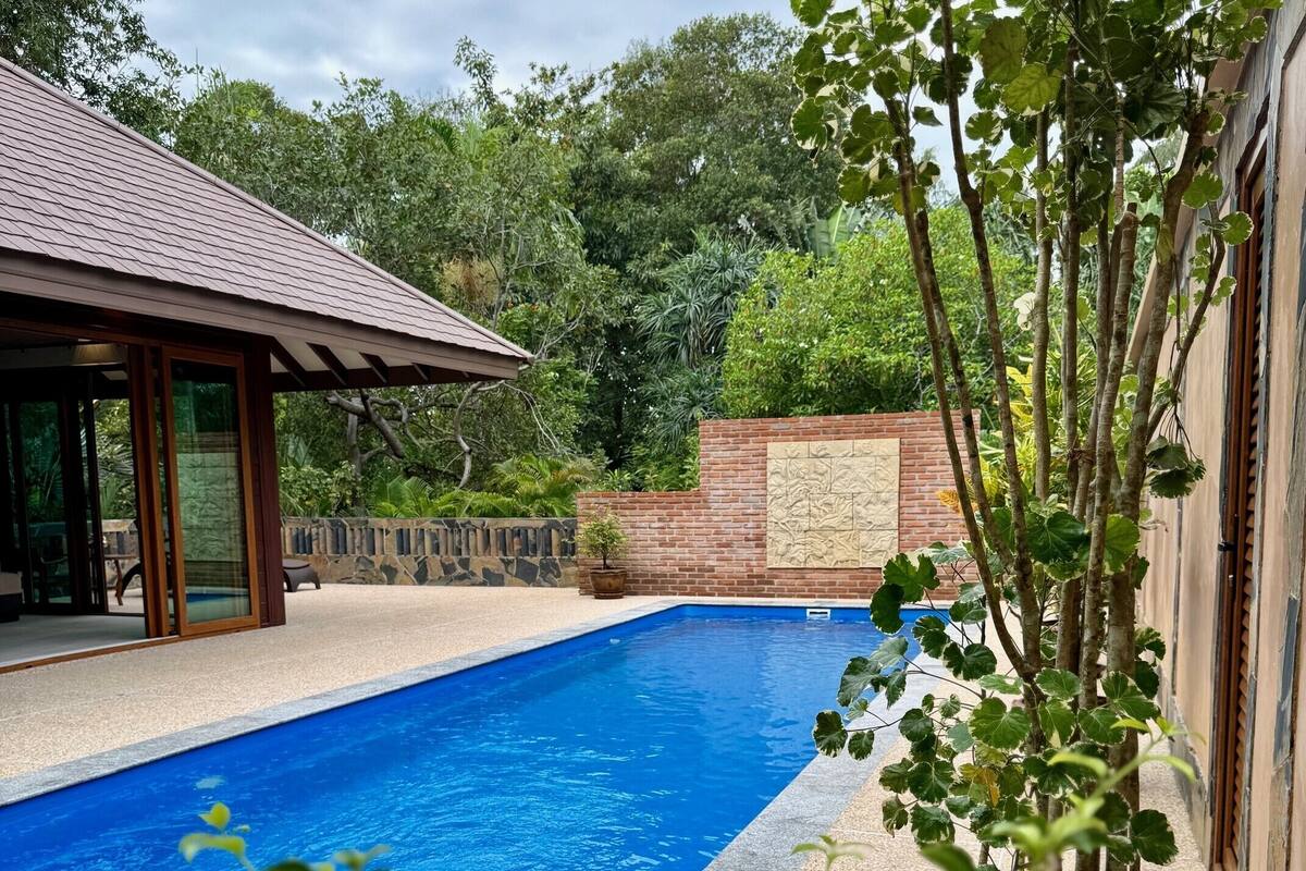 Une piscine dotée d’une terrasse carrelée, entourée d’un mur de briques et d’une végétation luxuriante.