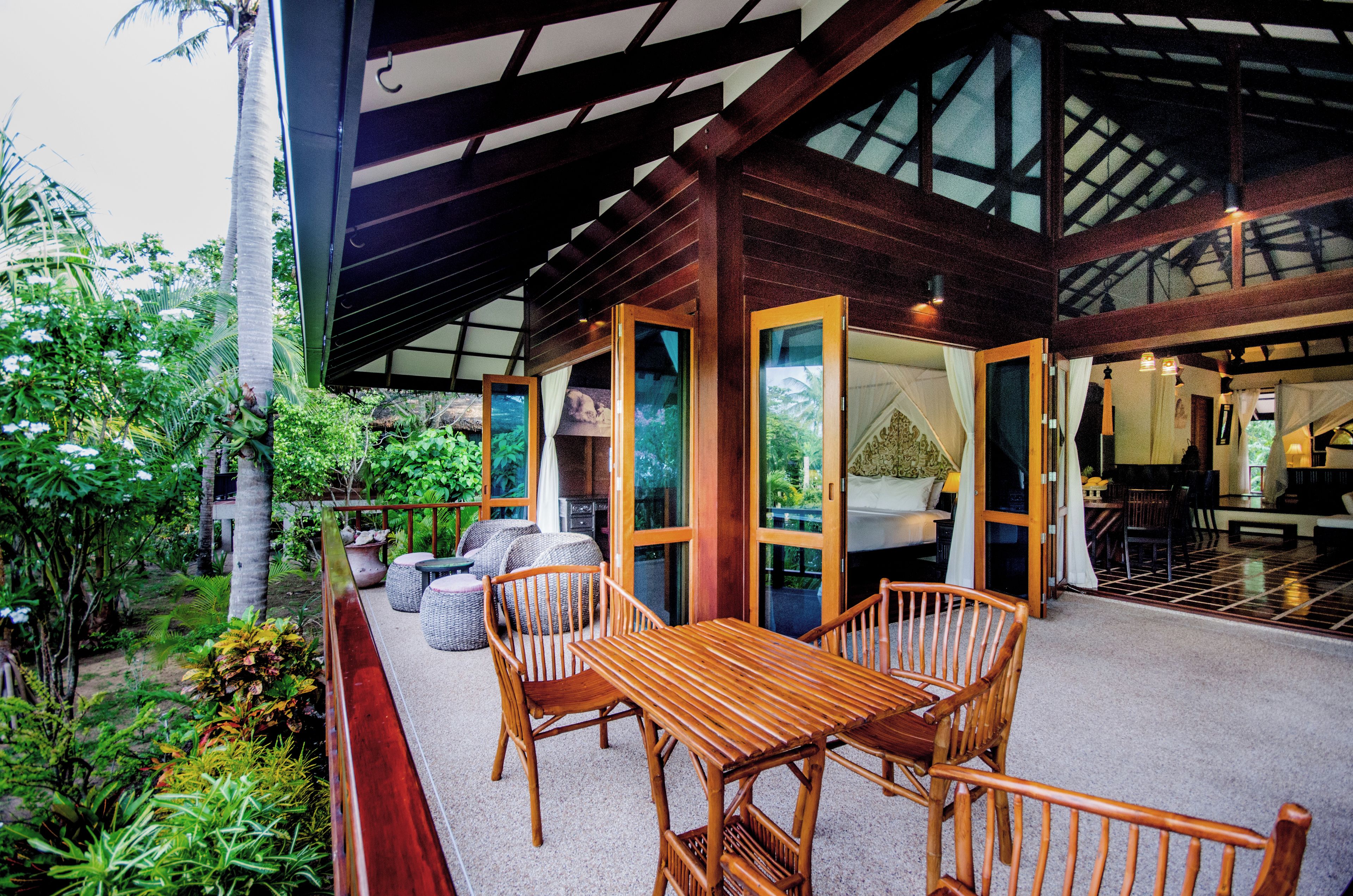 A wooden deck with a table and chairs, surrounded by lush greenery.