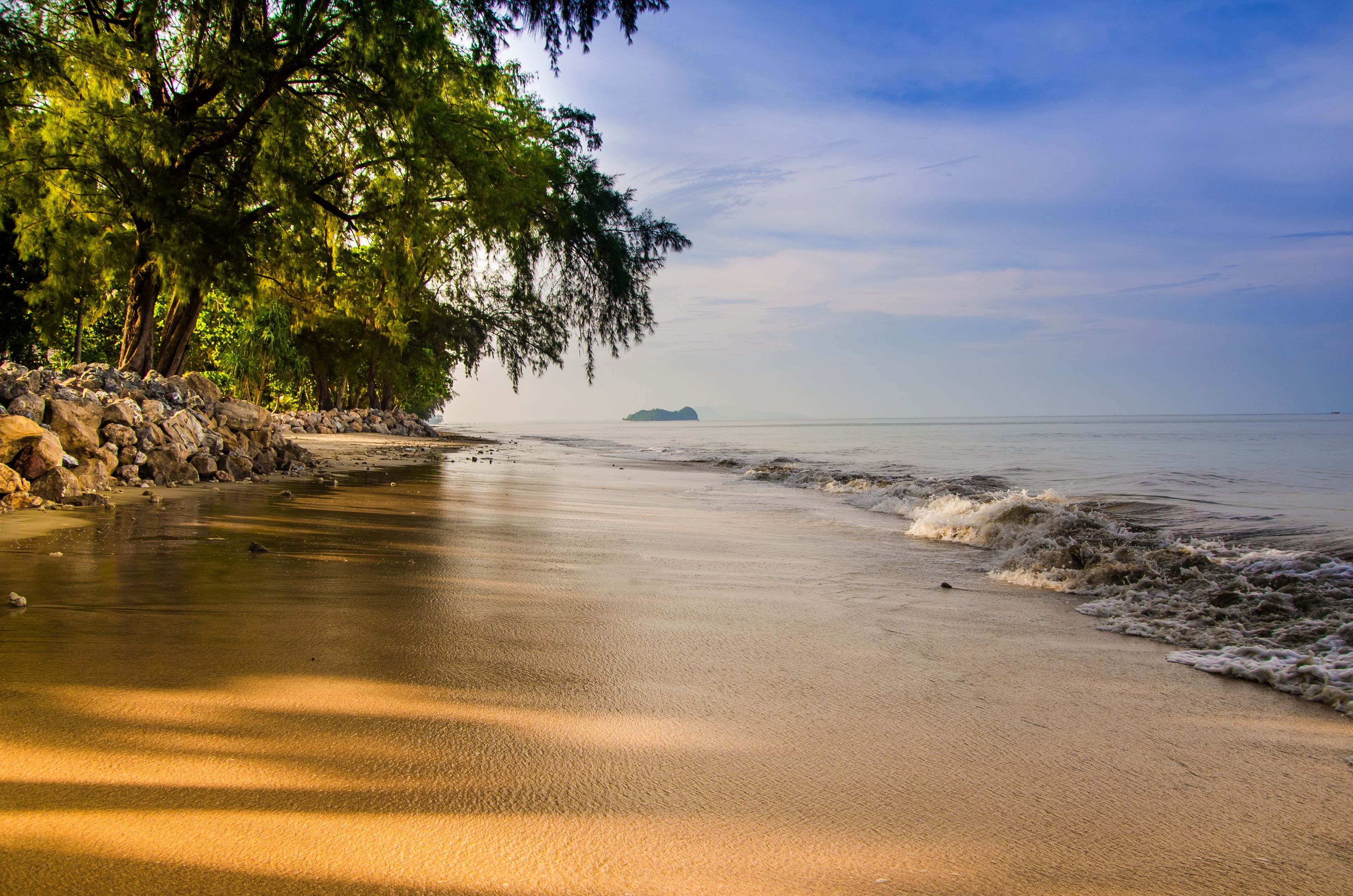 Una playa con costa rocosa, agua tranquila y una isla distante.