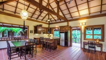 Una cocina amplia con vigas de madera, un comedor con una mesa grande y sillas, y vistas a zonas verdes.