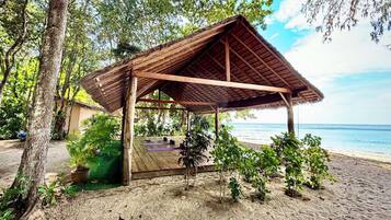A beachside wooden structure with a thatched roof, surrounded by greenery and overlooking the sea.