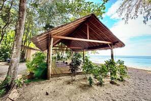 Une construction en bois située au bord de la plage, avec un toit de chaume, entourée de verdure et offrant une vue sur la mer.