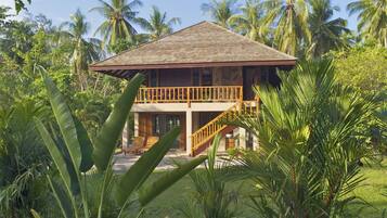 Casa de madera de dos pisos con balcón, rodeada de vegetación tropical.