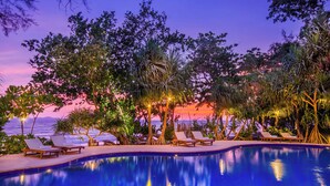 Un espace aménagé au bord de la piscine, avec des chaises longues et une vue sur l’océan au coucher du soleil.