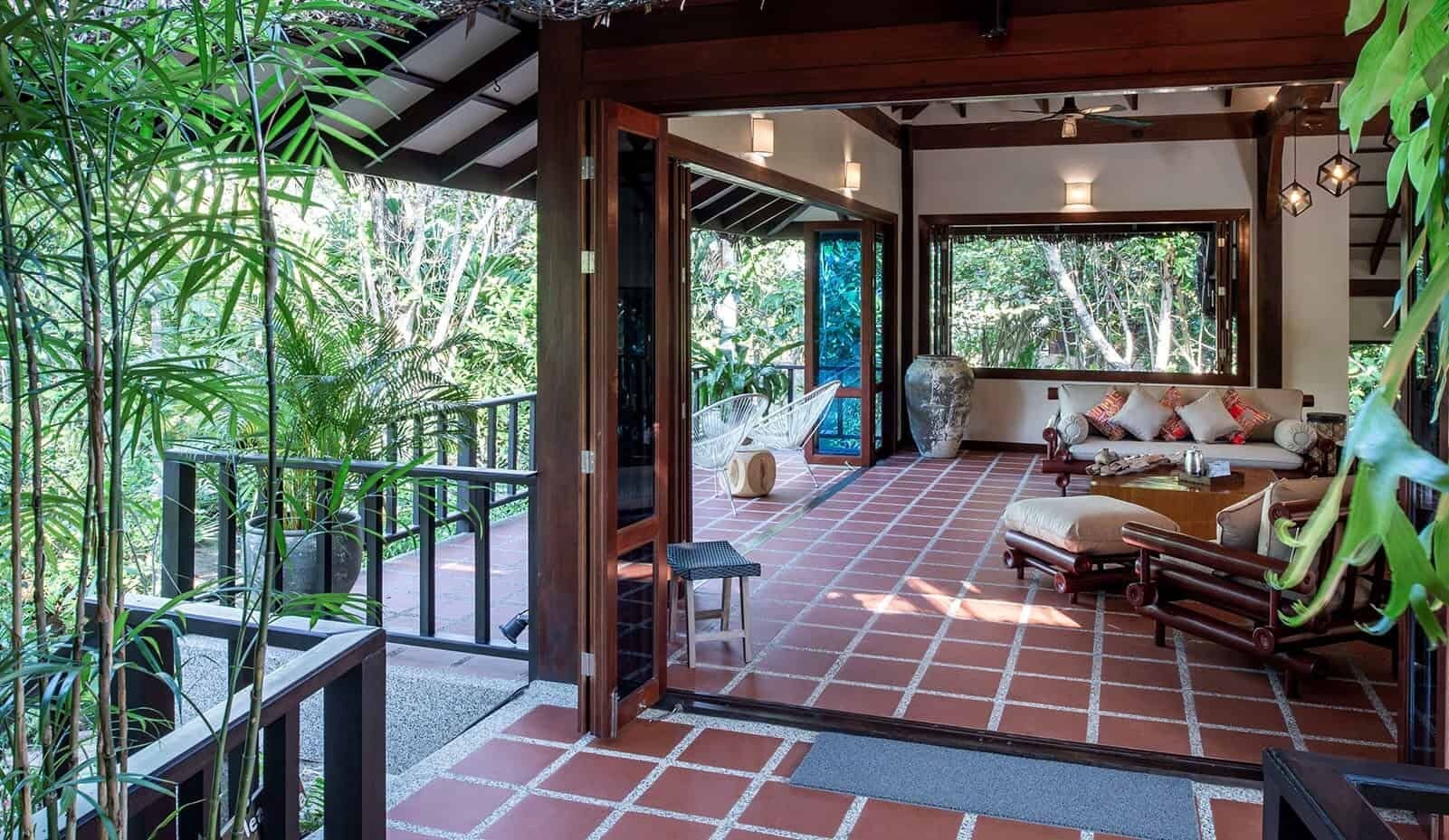 A spacious room with a tiled floor, a sofa set, and a view of lush greenery outside.