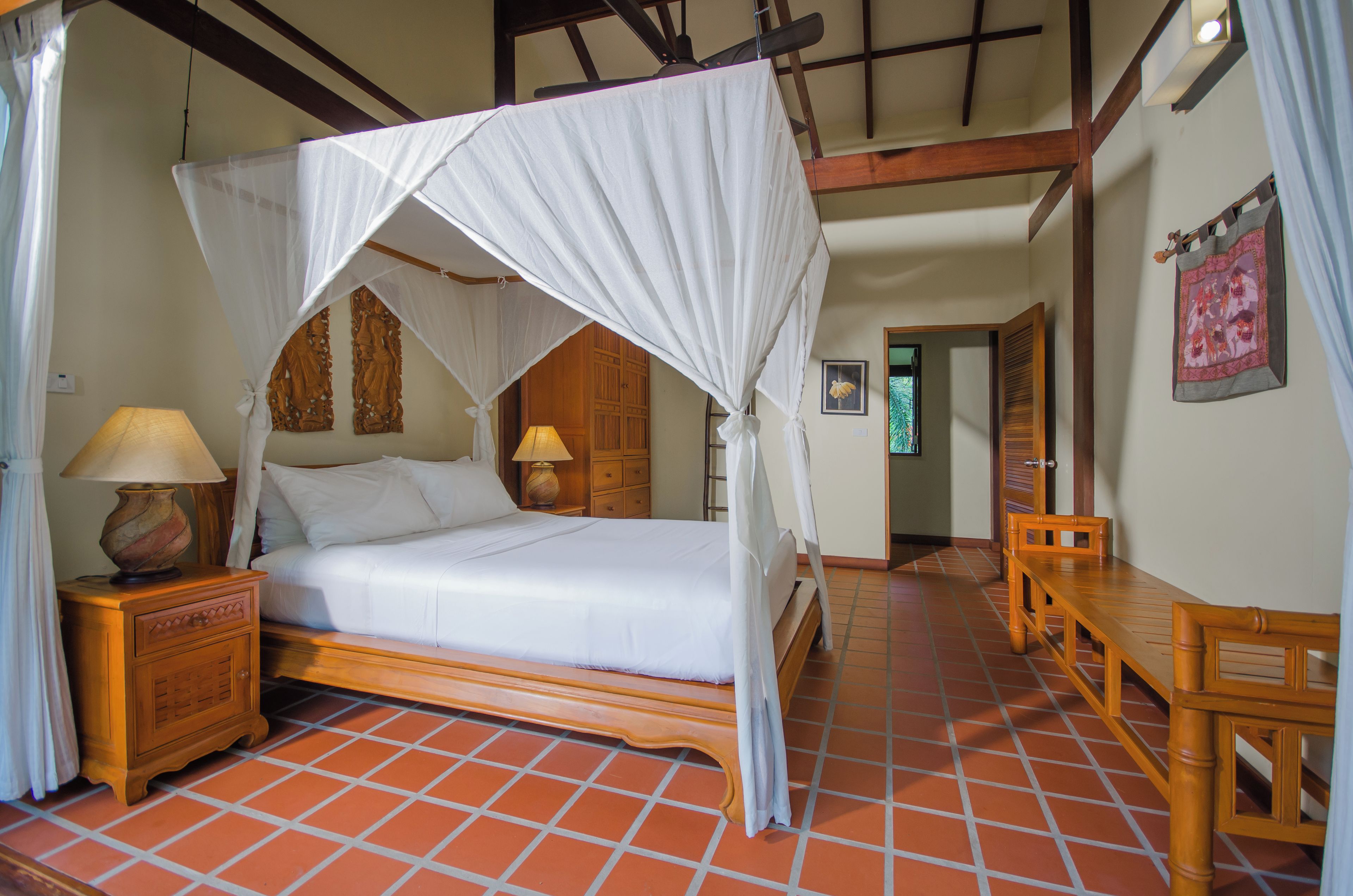 A room with a four-poster bed, wooden nightstands, a wooden bench, and a tiled floor.