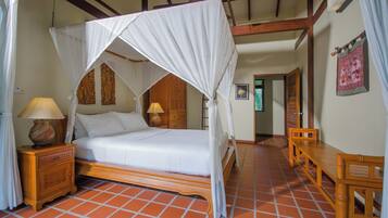 A room with a four-poster bed, wooden nightstands, a wooden bench, and a tiled floor.