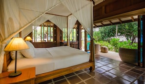 A bed with a canopy, a nightstand with a lamp, and a view of greenery outside.