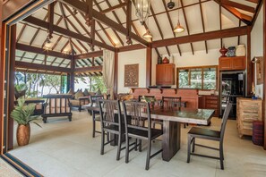 Un vaste espace à manger avec une grande table et des chaises en bois, une cuisine dotée de meubles en bois et un plafond avec des poutres apparentes.
