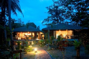 A two-story building with a thatched roof, surrounded by tropical vegetation. - Koh Jum Beach Villas (Nuea Khlong)