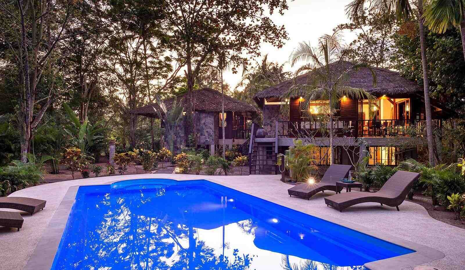 A poolside area with lounge chairs, a swimming pool, and a building with a thatched roof.