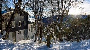 A two-story building with a dark exterior, surrounded by snow-covered trees and a mountainous backdrop. - Attunga Alpine Lodge and Apartments (Falls Creek)