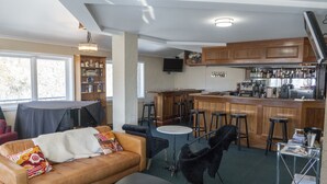 A cozy living room with a sofa, a coffee table, and a dog bed. There is a kitchen area with wooden cabinets and a bar counter. - Attunga Alpine Lodge and Apartments (Falls Creek)