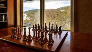 A chessboard set up on a wooden table in a room with a large window overlooking a mountainous landscape. - Attunga Alpine Lodge and Apartments (Falls Creek)