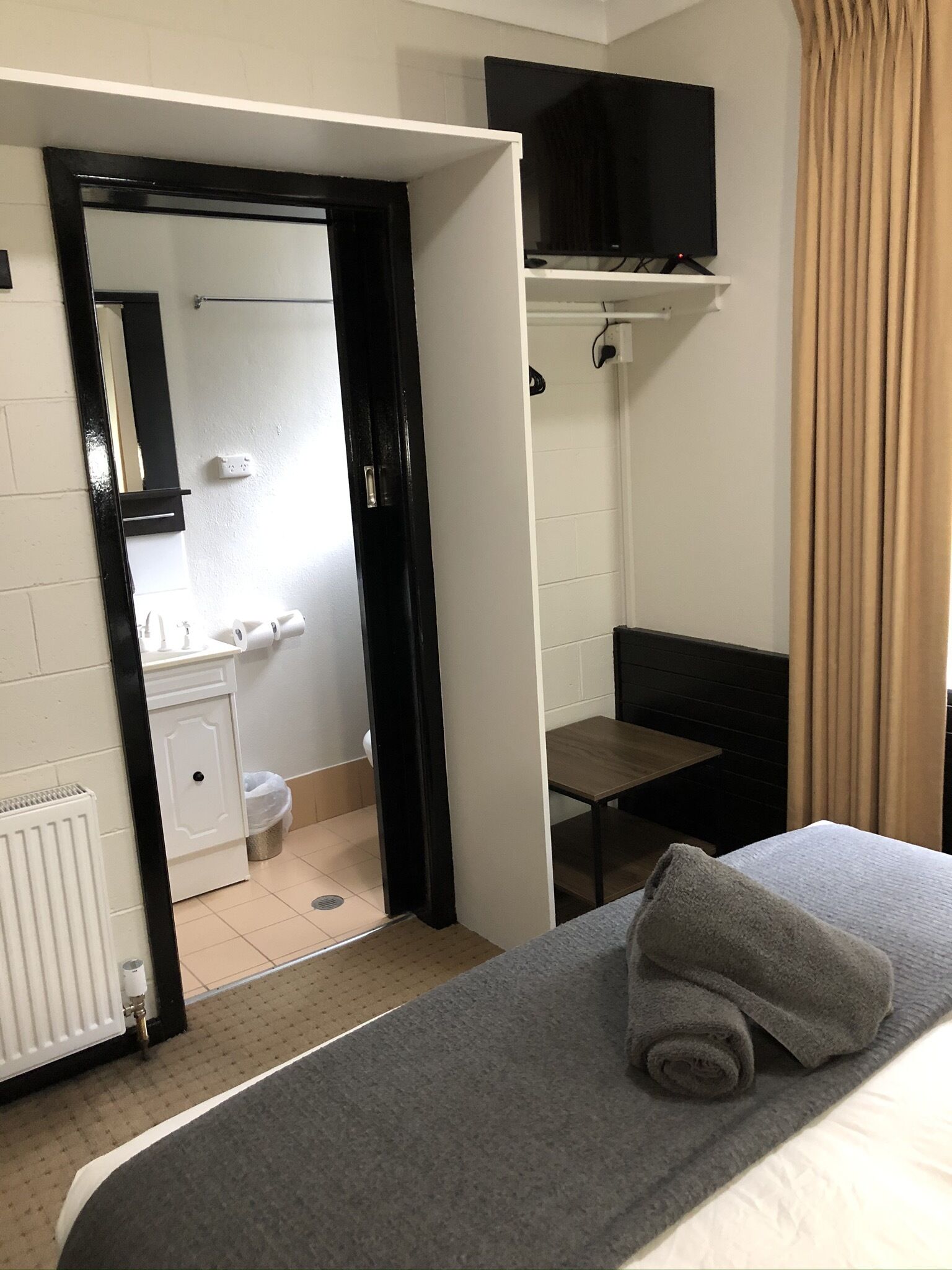 A hotel room with a bed, a small table, a TV on a shelf, and a bathroom visible through an open door.