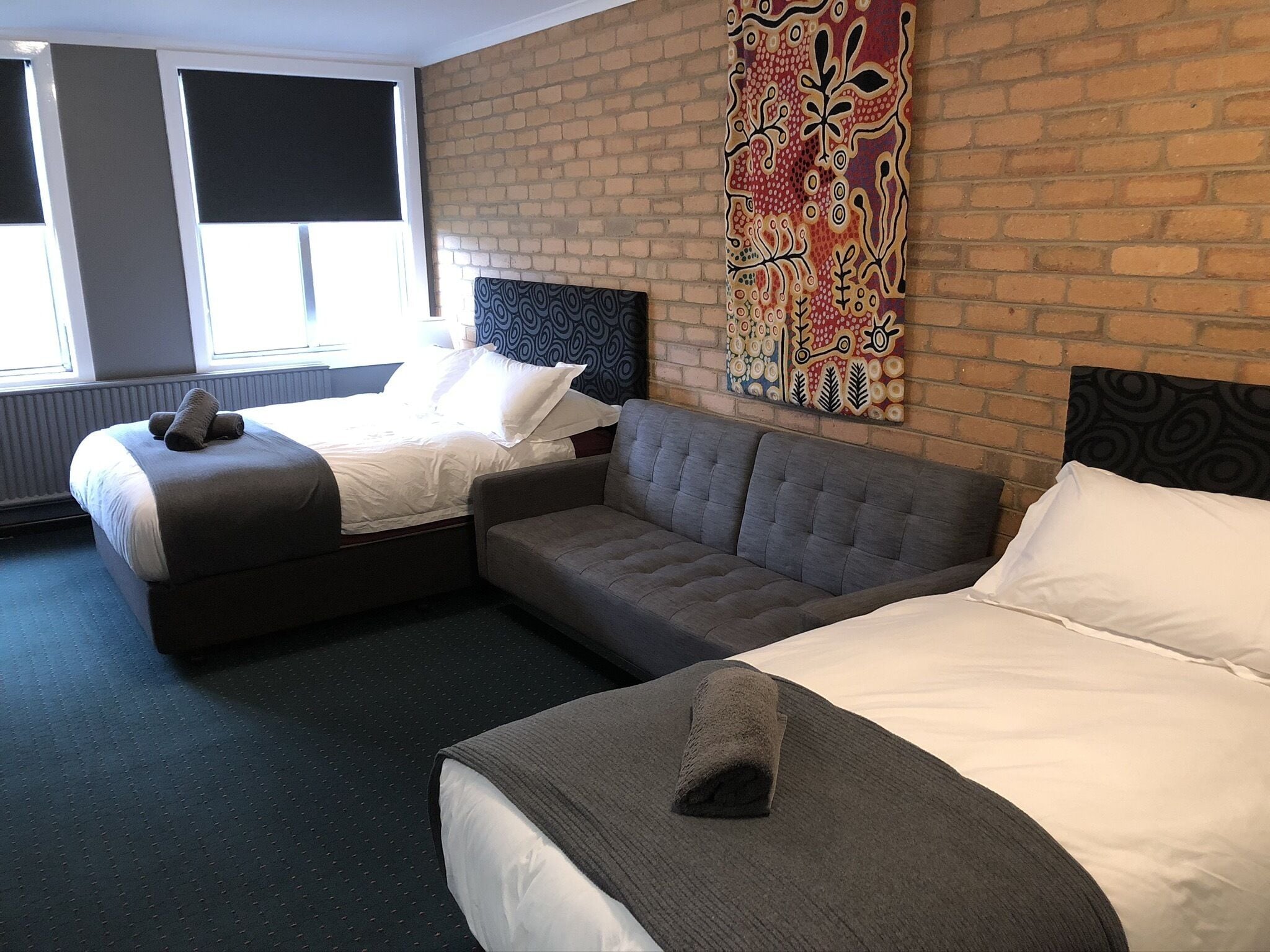 A hotel room with two beds, a grey sofa, and a large window.