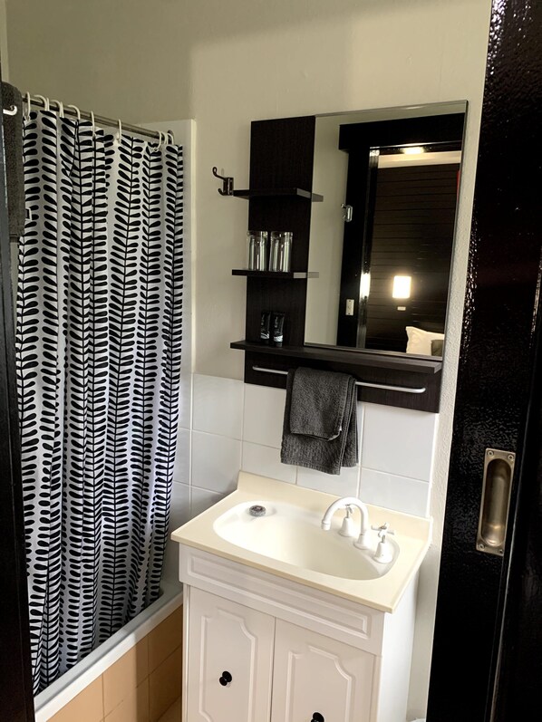 Un baño con lavamanos blanco, un espejo y una cortina de ducha con estampado de hojas.
