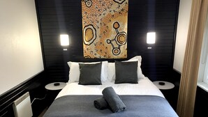A neatly made bed with a gray blanket and a rolled towel, two pillows, and a decorative wall piece above. - Attunga Alpine Lodge and Apartments (Falls Creek)