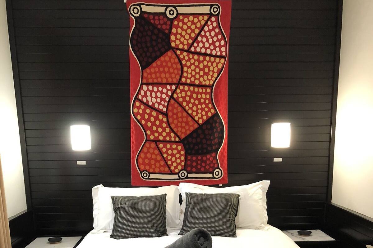 A hotel room with a large bed, two nightstands, a wall-mounted artwork, and two wall sconces.