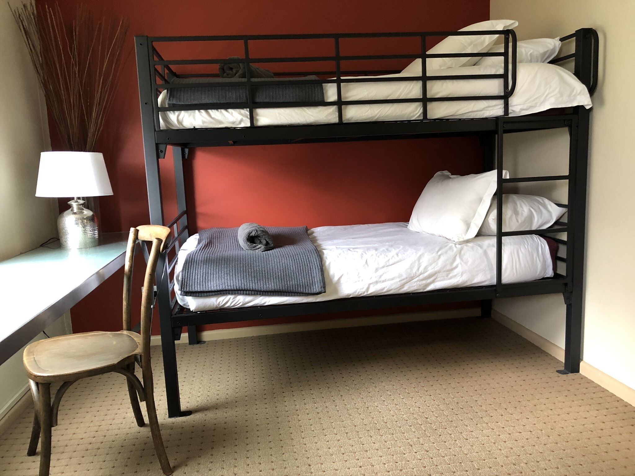 A bunk bed with a desk and chair, a lamp, and a vase with dried plants.
