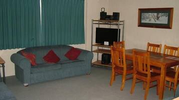 A living room with a sofa, a dining table with chairs, a TV on a stand, and a framed picture on the wall.
