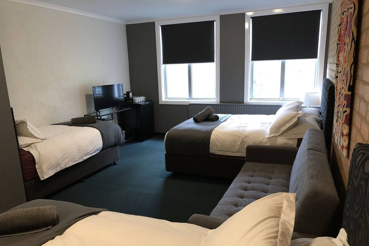 A hotel room with two single beds, a sofa, a TV, and a small table.