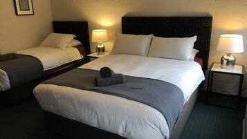 Habitación de hotel con dos camas, cada una con ropa de cama blanca y cabeceros oscuros. Hay dos mesitas de noche con lámparas y un cuadro en la pared.