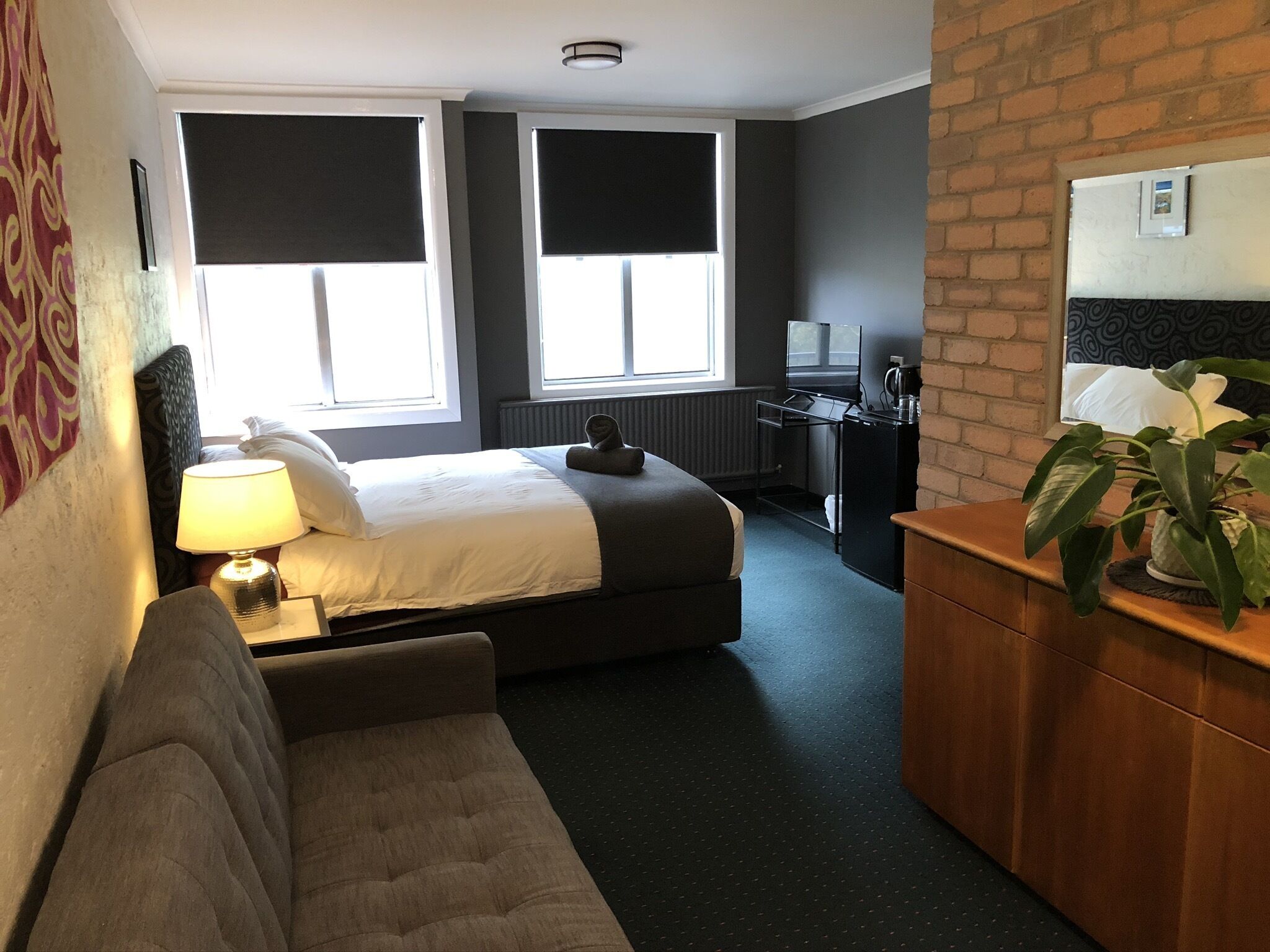 Una habitación de hotel con cama, escritorio, televisión, cafetera y una planta.