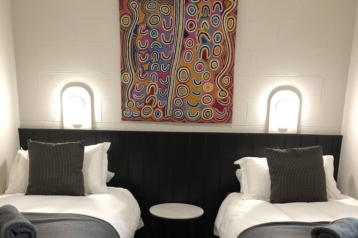 A hotel room with two beds, a small round table, and a colorful abstract painting on the wall.