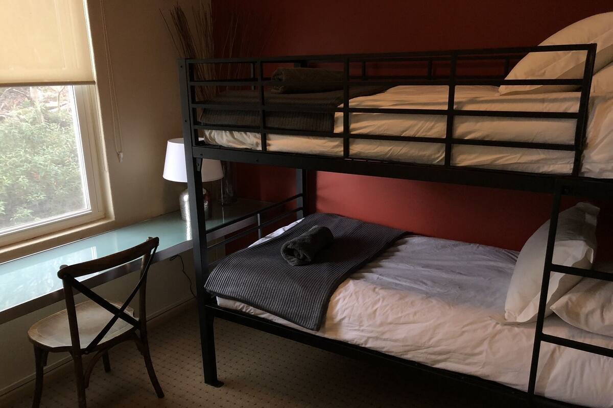 A bunk bed room with a window, a desk, and a chair.