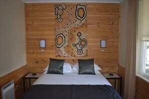 A bedroom with a wooden headboard, two bedside tables, a bed with pillows, and a wall tapestry. - Attunga Alpine Lodge and Apartments (Falls Creek)