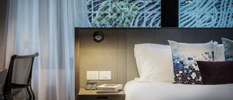 A hotel room with a bed, a nightstand, a chair, and a window with a view of trees.