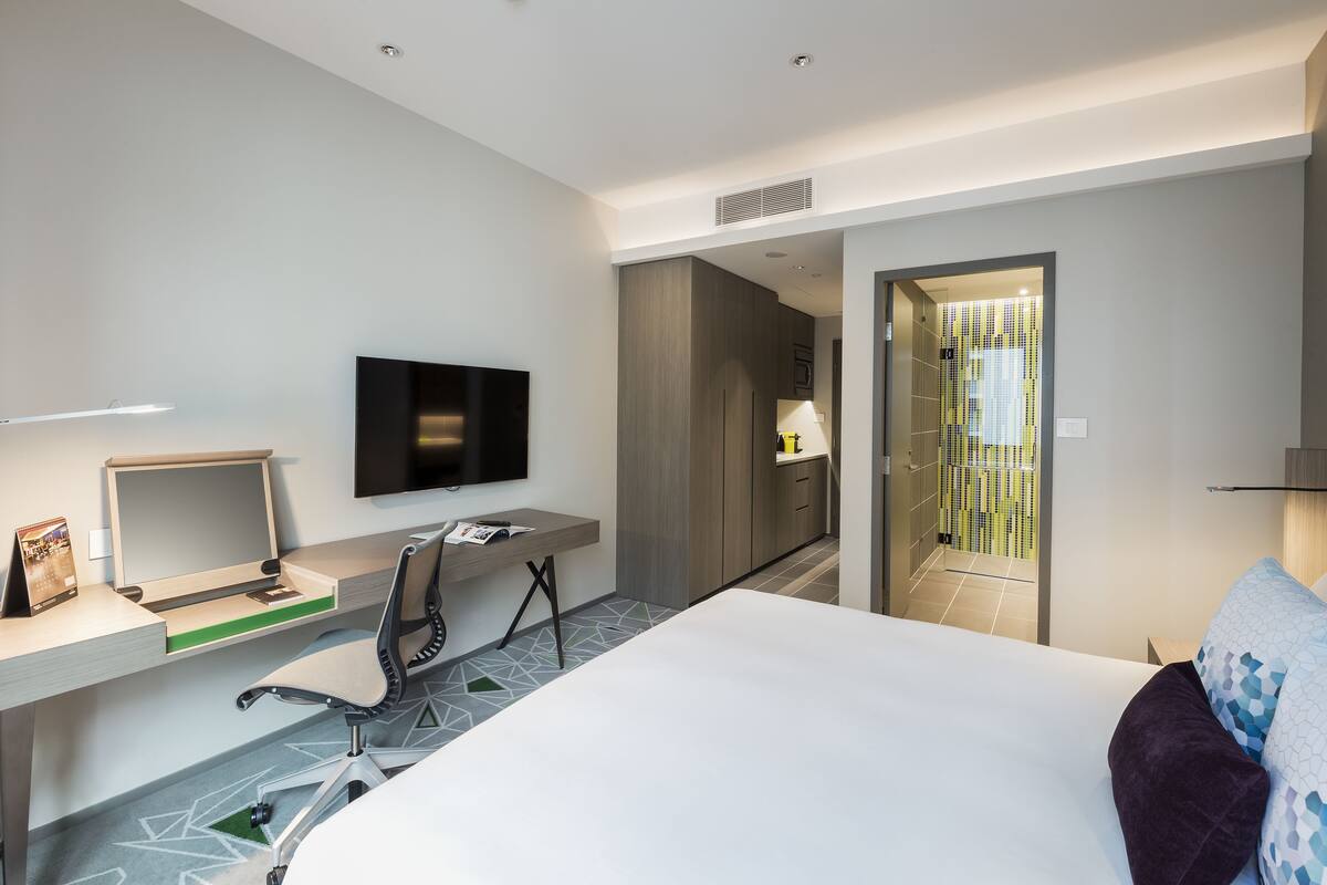 Habitación de hotel moderna con cama, escritorio, silla, televisor y vista al baño.