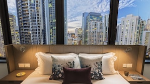 A hotel room with a large bed, two nightstands, and a view of a cityscape through large windows. - Capri by Fraser, Brisbane (Brisbane)