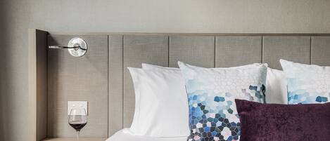 A hotel room with a bed, a nightstand, a wine glass, and a cityscape artwork on the wall.