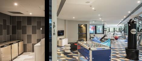 A modern hotel lobby with a foosball table, a punching bag, and a fitness area with exercise equipment.