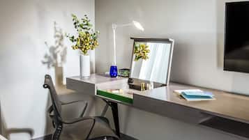 Una scrivania moderna con una sedia, una lampada da tavolo, un vaso con fiori, uno specchio e una TV a schermo piatto.