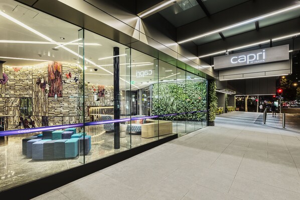 A modern retail store with glass walls, a green wall with plants, and a sign reading "capri by Fraser".