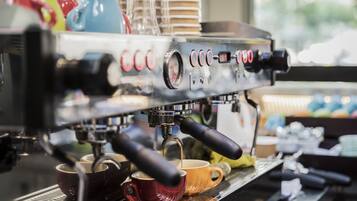 A coffee machine with multiple buttons and a digital display, cups placed below it, and a window in the background.