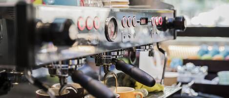 A coffee machine with multiple buttons and a digital display, cups placed below it, and a window in the background.