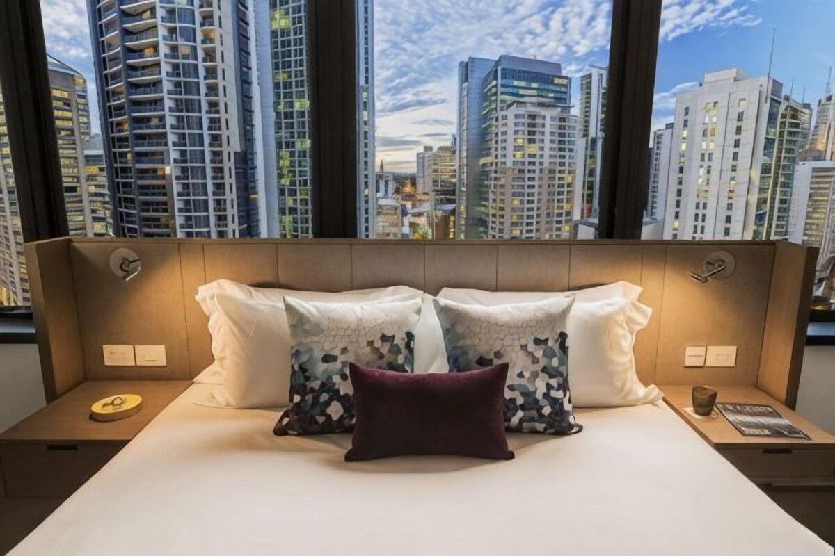 A hotel room with a large bed, two nightstands, and a view of tall buildings.