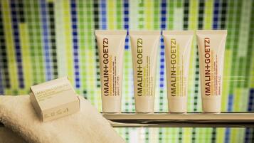 Four tubes of MALIN+GOETZ body wash and shampoo on a shelf with a checkered tile background.