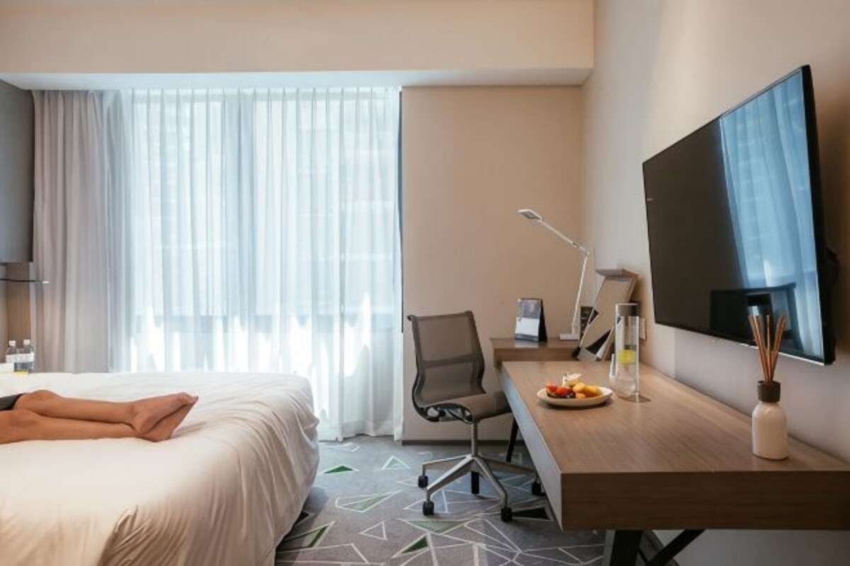 A hotel room with a bed, a desk, a chair, a TV, and a window with curtains.