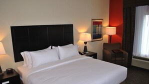 Ein Hotelzimmer mit einem großen Bett, zwei Nachttischen mit Lampen, einem Sessel und einem Bild an der Wand.