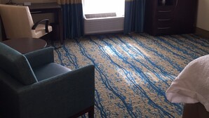 A hotel room with a desk, chair, TV, and a large window with curtains.