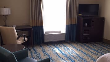 Habitación de hotel con escritorio, silla, televisor y una ventana grande con cortinas.